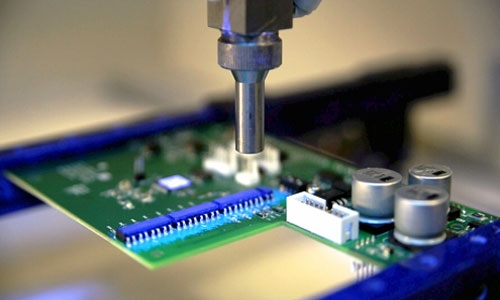 Applying conformal coating to a printed circuit board through spraying.